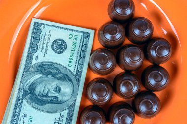 Turuncu bir tabağın üstünde çikolatalı şekerler ve nakit parayla.