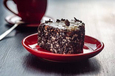 Kırmızı bir tabakta çikolata parçaları serpiştirilmiş kalp şeklinde lezzetli bir pasta. Ahşap bir arka planda yakın plan çekilmiş..