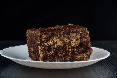 Bir parça çikolatalı kek, beyaz bir tabakta, siyah bir tahta sırtında.