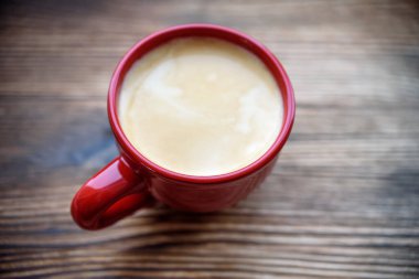 Ahşap bir masada kırmızı bir bardak kapuçino. 