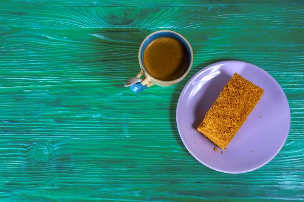 A piece of cake and a cup of coffee on a green wooden background.