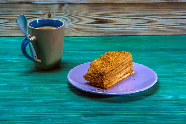 A piece of cake and a cup of coffee on a green wooden background.