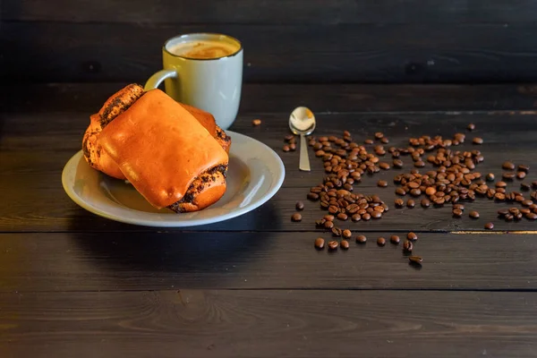 Buns with poppy seeds on a gray plate and coffee mug on a black wooden background. Near coffee beans