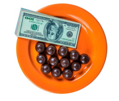 Turuncu bir tabağın üstünde çikolatalı şekerler ve nakit parayla.