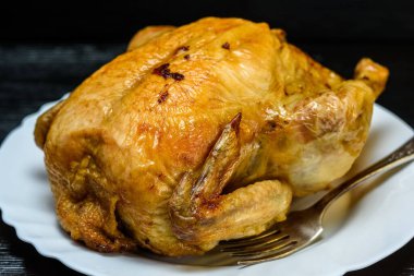 Beyaz tabakta kızarmış tavuk, siyah ahşap arka planda.