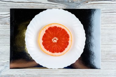 Tahta bir arka planda beyaz bir tabakta taze bir greyfurt.