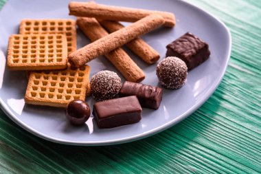 Yeşil ahşap bir arka planda duran, btruzy bir tabakta kurabiyeler ve çikolatalar..