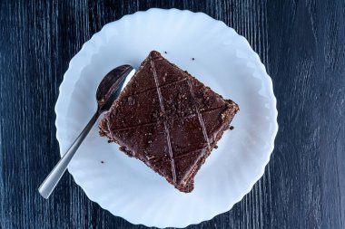 Bir parça çikolatalı kek, beyaz bir tabakta, siyah bir tahta sırtında.