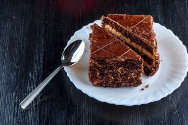 Bir parça çikolatalı kek, beyaz bir tabakta, siyah bir tahta sırtında.