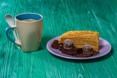 Bir parça kek ve bir tabakta çikolata, yanında bir fincan kahve, yeşil ahşap bir arka planda yakın plan fotoğrafı..