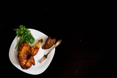 Siyah bir arka planda, tabakta pişmiş tavuk.