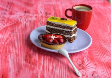 Çilekli bir kek ve tabakta pofuduk bir bisküvi, fincanda kahvenin yanında, ahşap bir arka planda fotoğraflanmış..