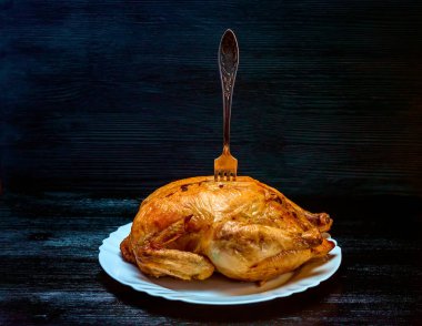 Beyaz tabakta kızarmış tavuk, siyah ahşap arka planda.