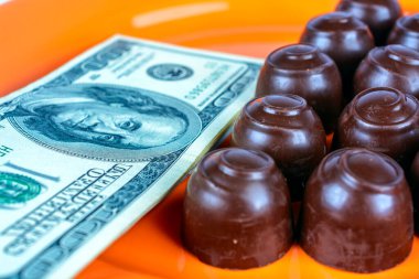 Turuncu bir tabağın üstünde çikolatalı şekerler ve nakit parayla.