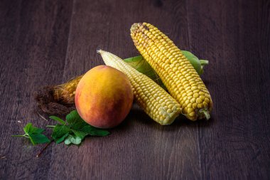 Şeftali ve mısır koçanları koyu ahşap arka planda.