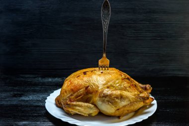 Beyaz tabakta kızarmış tavuk, siyah ahşap arka planda.