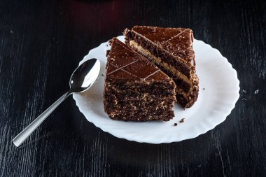 Bir parça çikolatalı kek, beyaz bir tabakta, siyah bir tahta sırtında.