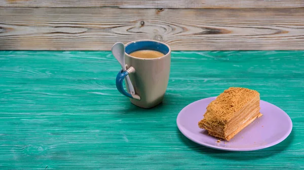 A piece of cake and a cup of coffee on a green wooden background.