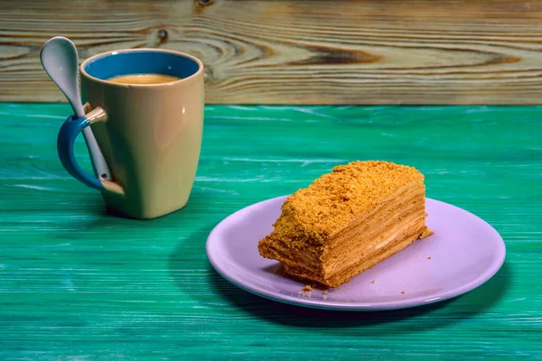 A piece of cake and a cup of coffee on a green wooden background.