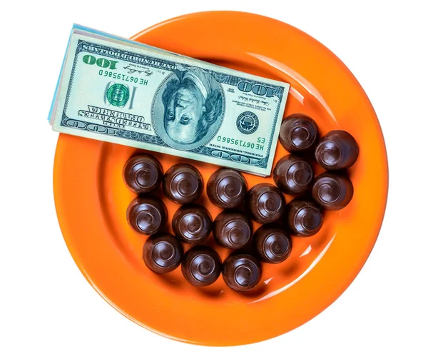 Turuncu bir tabağın üstünde çikolatalı şekerler ve nakit parayla.