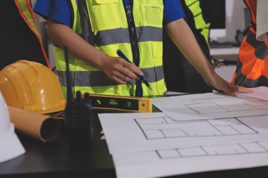 Endüstriyel mühendislerden oluşan bir ekip, fabrikadaki masada bulunan makine planlarını analiz ediyor. Fabrikada ya da üretim tesisinde çalışıyorum..