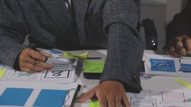 Genç iş adamı iş yerindeki kağıda yapışkan notlar yazarken kağıda yazı yazıyor.