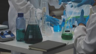 Laboratuvar önlüklü bilim adamı elinde cam tüp tutarken laboratuvarda sıvı üretiyor.