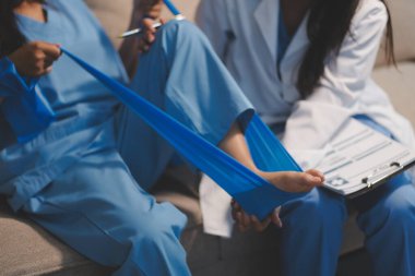 Kendine güvenen fizyoterapist, hastanın bacağını klinik odasında gerdirerek direnç bandı kullanmasına yardım ediyor..