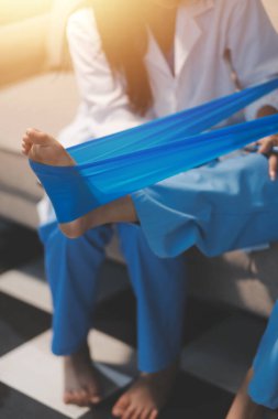 Kendine güvenen fizyoterapist, hastanın bacağını klinik odasında gerdirerek direnç bandı kullanmasına yardım ediyor..