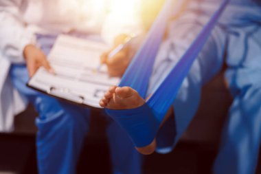 Kendine güvenen fizyoterapist, hastanın bacağını klinik odasında gerdirerek direnç bandı kullanmasına yardım ediyor..