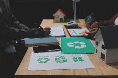 Ekip toplantısında, ESG konu sunumu için dizüstü bilgisayar kullanan Asyalı kadın, çok ırklı iş adamlarından oluşan genç bir gruba liderlik ediyor. Sürdürülebilir iş uygulaması, insanlar ev konseptinde çalışıyor