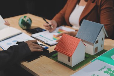 Ekip toplantısında, ESG konu sunumu için dizüstü bilgisayar kullanan Asyalı kadın, çok ırklı iş adamlarından oluşan genç bir gruba liderlik ediyor. Sürdürülebilir iş uygulaması, insanlar ev konseptinde çalışıyor