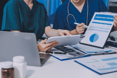 Two doctors and a female nurse meet at a table in the hospital, collaborating on medical tasks using laptops and computers