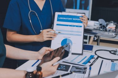 Two doctors and a female nurse meet at a table in the hospital, collaborating on medical tasks using laptops and computers