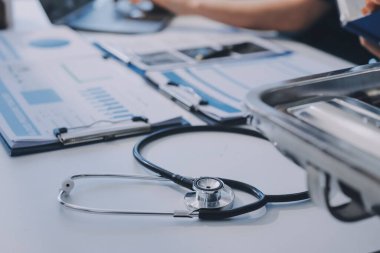 Two doctors and a female nurse meet at a table in the hospital, collaborating on medical tasks using laptops and computers