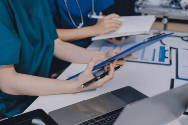Two doctors and a female nurse meet at a table in the hospital, collaborating on medical tasks using laptops and computers
