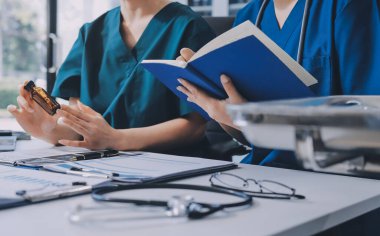 Two doctors and a female nurse meet at a table in the hospital, collaborating on medical tasks using laptops and computers