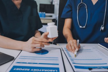 Medical team meeting analyzing blood test results in hospital laboratory. Doctors and scientists in lab coats are having a discussion about blood test result, holding test tubes and taking notes.