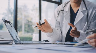 Medical team meeting analyzing blood test results in hospital laboratory. Doctors and scientists in lab coats are having a discussion about blood test result, holding test tubes and taking notes.