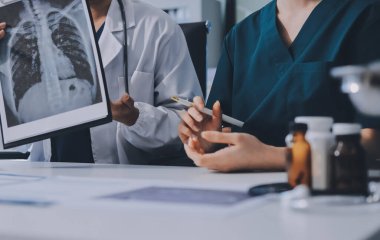 Medical team meeting analyzing blood test results in hospital laboratory. Doctors and scientists in lab coats are having a discussion about blood test result, holding test tubes and taking notes.