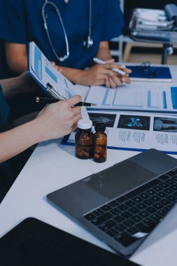 Two doctors and a female nurse meet at a table in the hospital, collaborating on medical tasks using laptops and computers