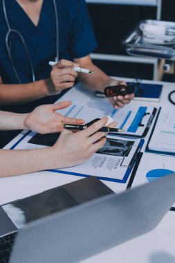 Two doctors and a female nurse meet at a table in the hospital, collaborating on medical tasks using laptops and computers