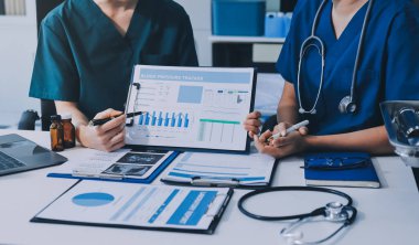 Two doctors and a female nurse meet at a table in the hospital, collaborating on medical tasks using laptops and computers