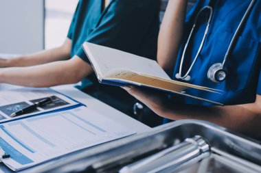 Two doctors and a female nurse meet at a table in the hospital, collaborating on medical tasks using laptops and computers