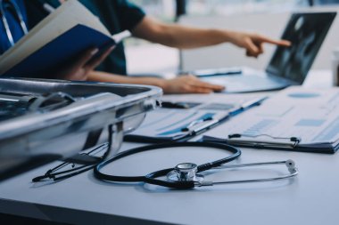 Two doctors and a female nurse meet at a table in the hospital, collaborating on medical tasks using laptops and computers