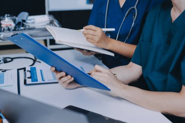 Two doctors and a female nurse meet at a table in the hospital, collaborating on medical tasks using laptops and computers