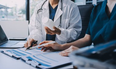 Medical team meeting analyzing blood test results in hospital laboratory. Doctors and scientists in lab coats are having a discussion about blood test result, holding test tubes and taking notes.