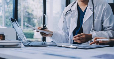 Medical team meeting analyzing blood test results in hospital laboratory. Doctors and scientists in lab coats are having a discussion about blood test result, holding test tubes and taking notes.