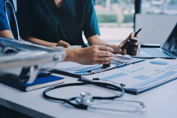 Two doctors and a female nurse meet at a table in the hospital, collaborating on medical tasks using laptops and computers