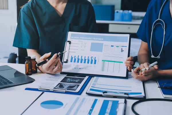 Two doctors and a female nurse meet at a table in the hospital, collaborating on medical tasks using laptops and computers